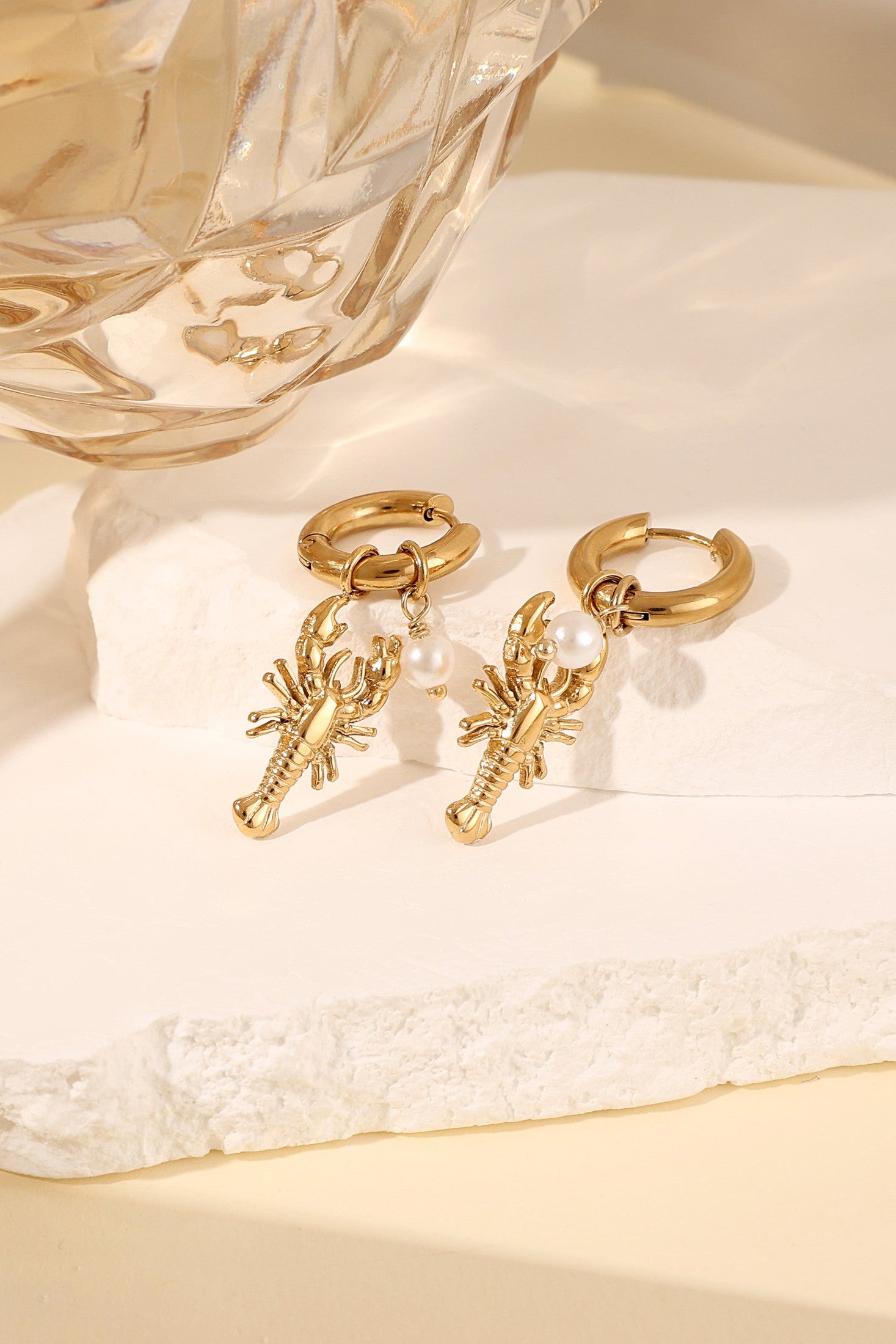 Stylish gold lobster drop earrings with pearl accent displayed on white stone block