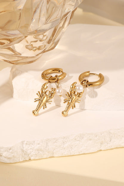Stylish gold lobster drop earrings with pearl accent displayed on white stone block