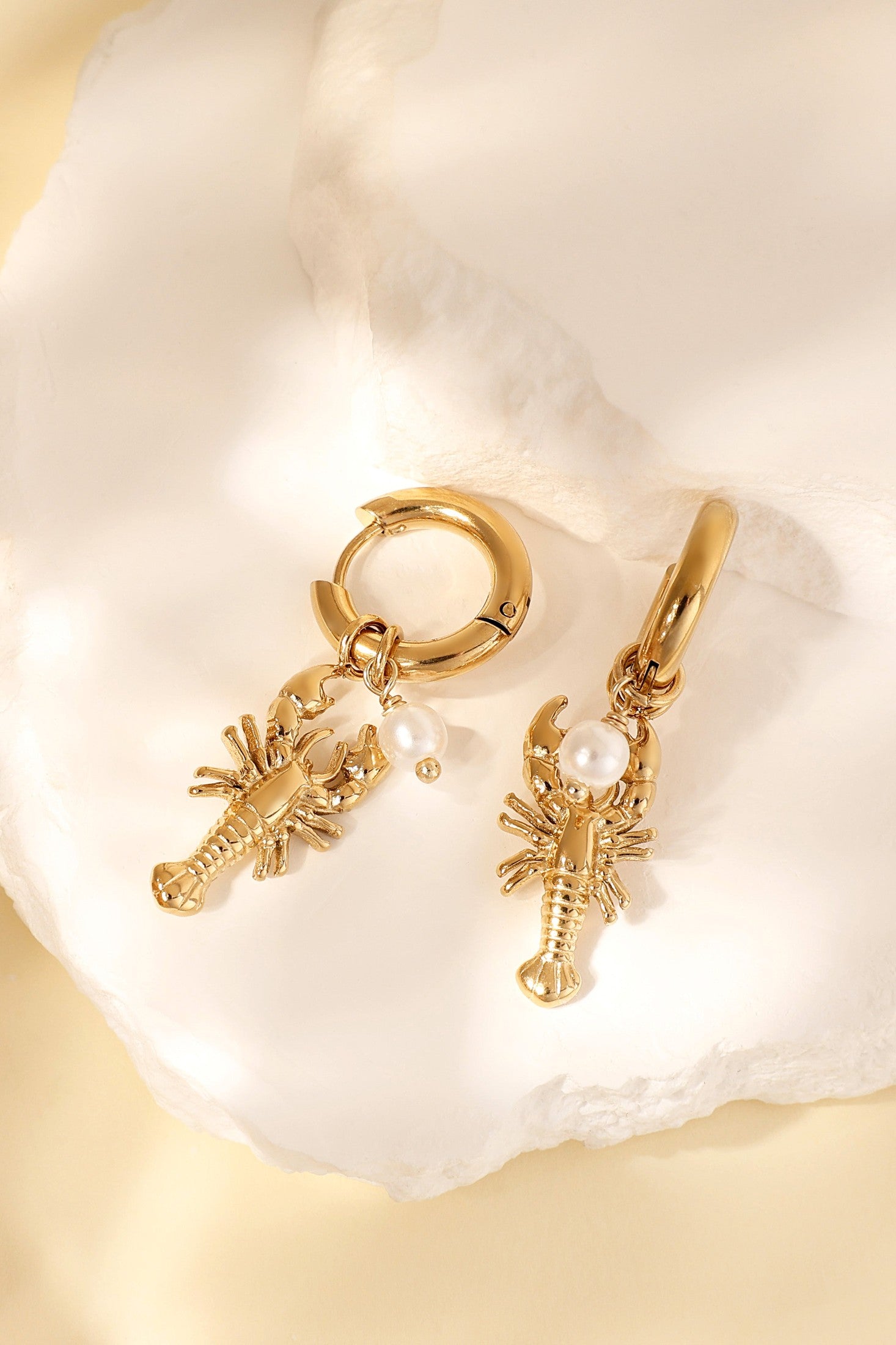 Close-up of gold lobster charm earrings with pearl on white textured stones
