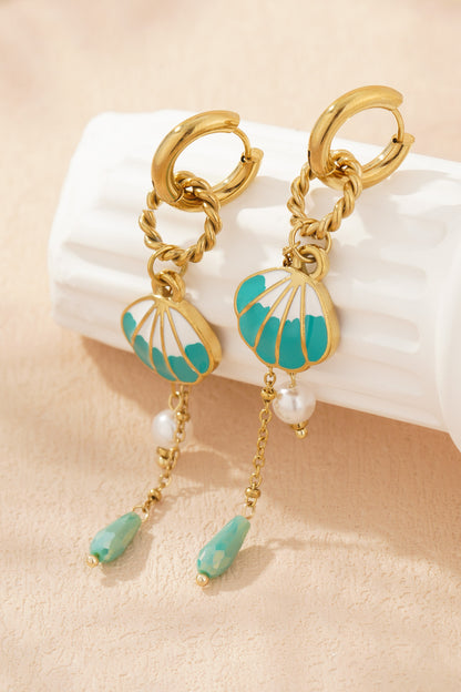 Shell charm drop earrings resting on textured cream background highlighting gold-tone shine, turquoise enamel shell and pearl bead details