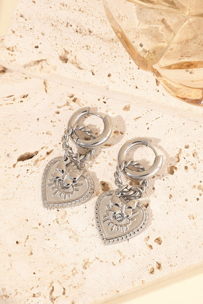 Silver heart charm hoop earrings placed on beige textured stone with warm lighting
