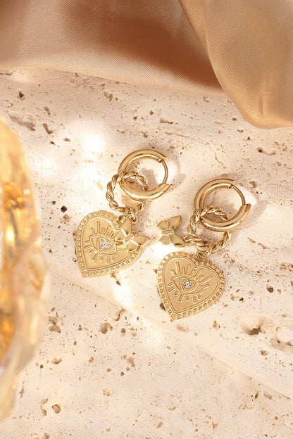 Gold heart charm hoop earrings lying on textured cream stone surface with sunlight
