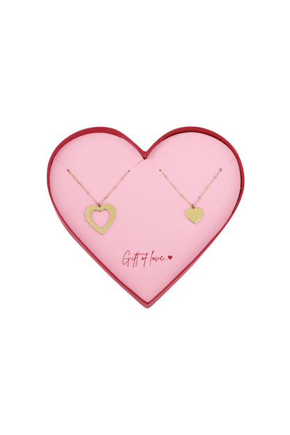 Two gold-tone heart necklaces with delicate chains displayed on a pink heart-shaped card inside a red-edged heart-shaped box reading 'Gift of love...'
