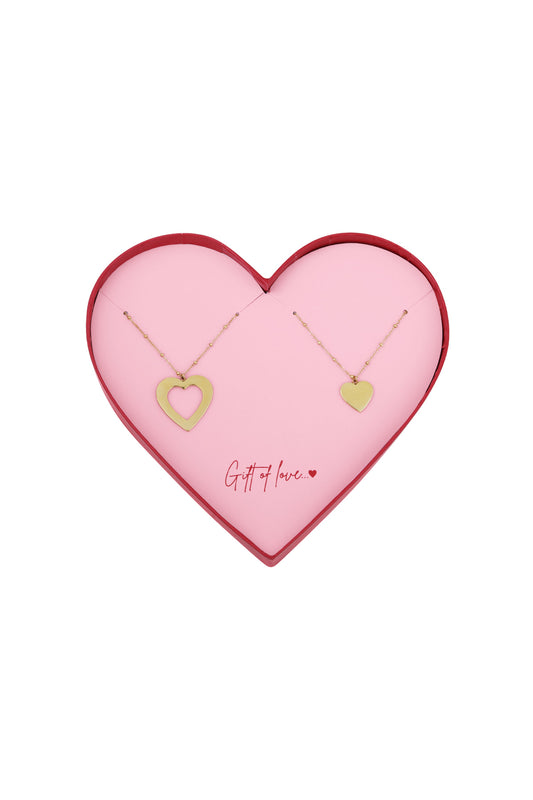 Two gold-tone heart necklaces with delicate chains displayed on a pink heart-shaped card inside a red-edged heart-shaped box reading 'Gift of love...'