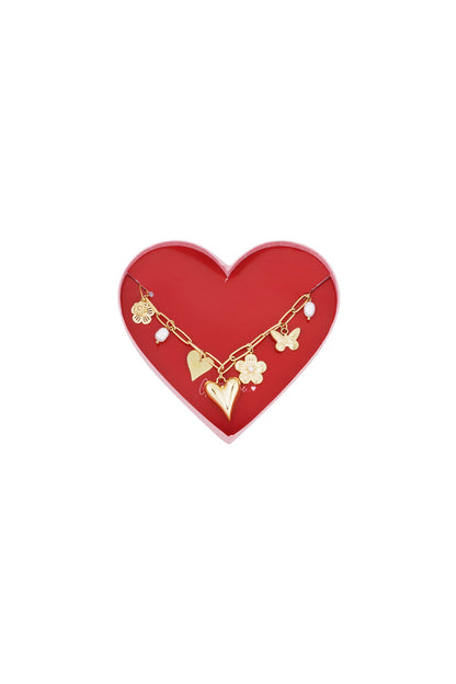 Golden charm link bracelet displayed on a red heart-shaped box featuring flower, butterfly, heart charms and pearl accents