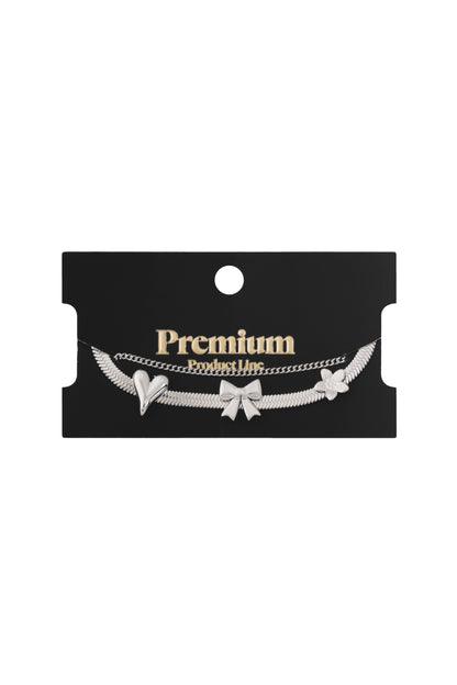 Silver charm bracelet with bow, heart, and flower charms displayed on black Premium Product Line card