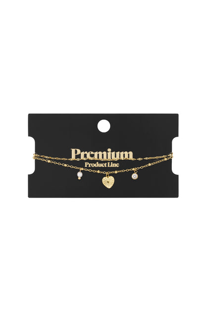 Gold charm bracelet with heart, pearl and crystal charms displayed on black premium product card