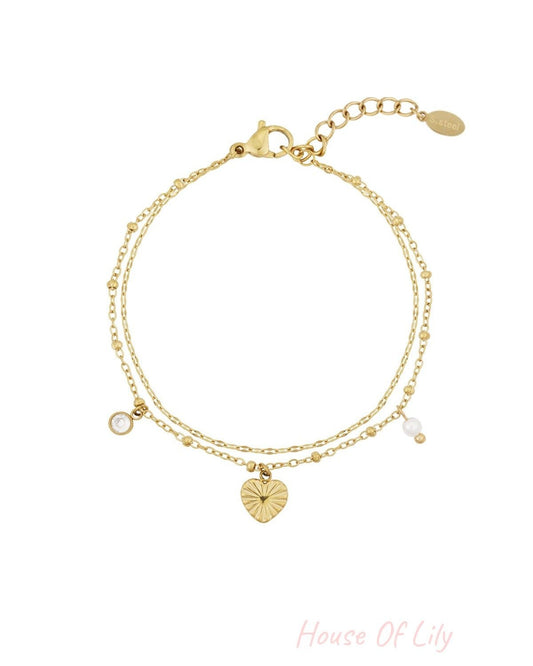 Gold stainless steel double-chain bracelet with a sunburst heart charm, a clear crystal, and a small pearl charm.