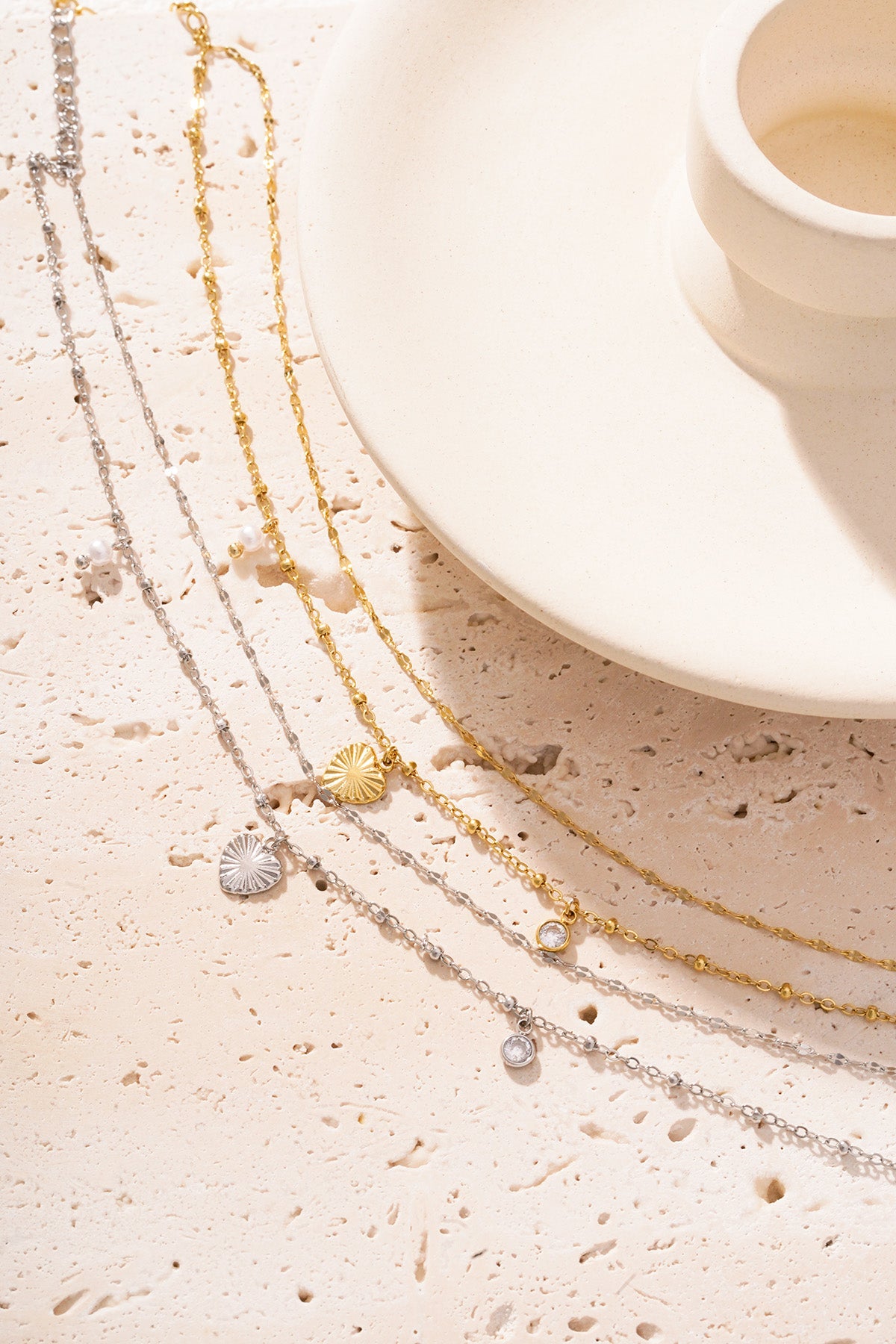 Silver and gold charm bracelets with heart, pearl and crystal details arranged on textured stone and cream plate