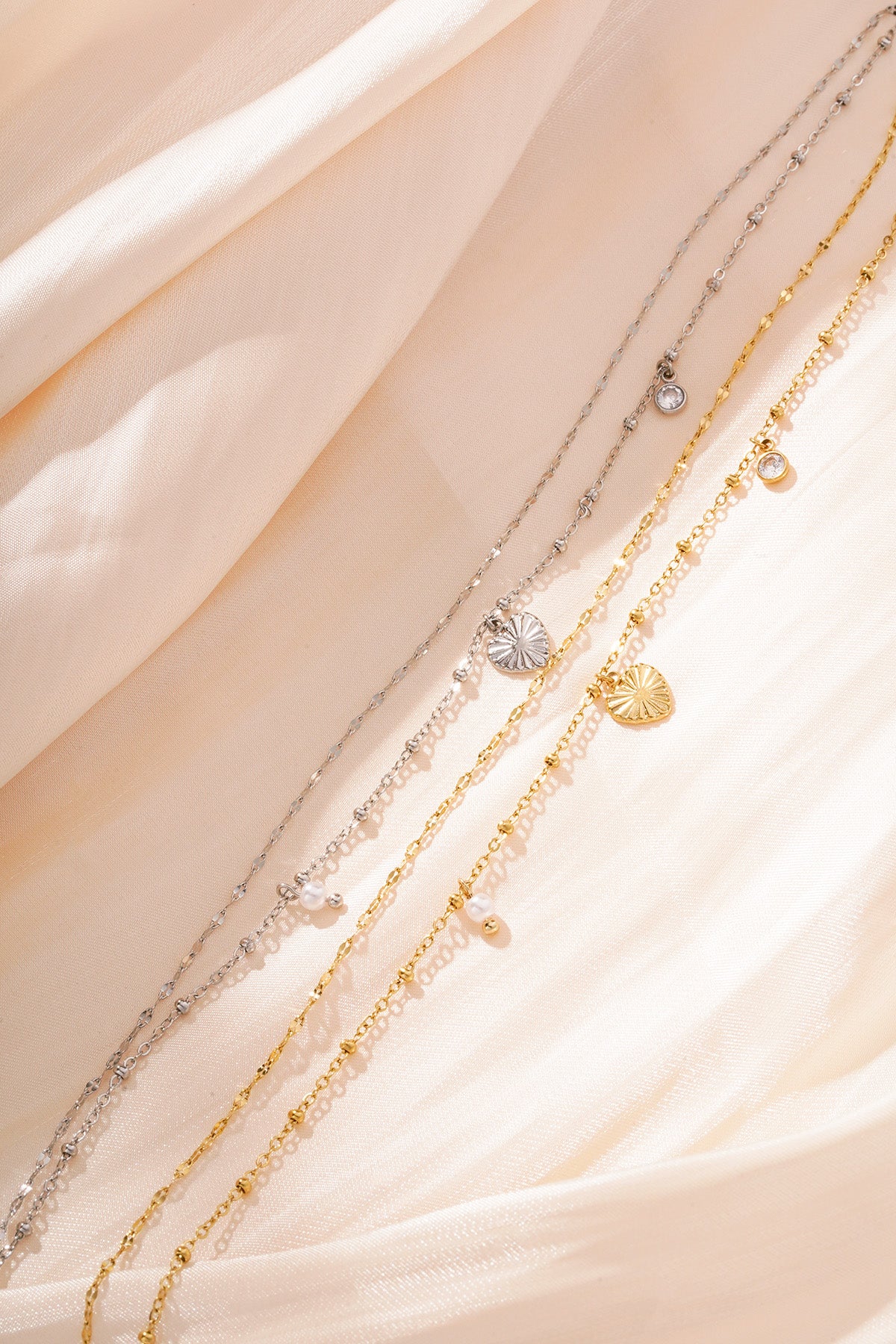 Close-up of silver and gold charm bracelets with heart, pearl and crystal charms on soft peach fabric