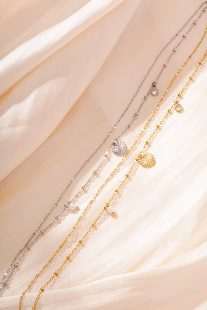 Close-up of silver and gold charm bracelets with heart, pearl and crystal charms on soft peach fabric