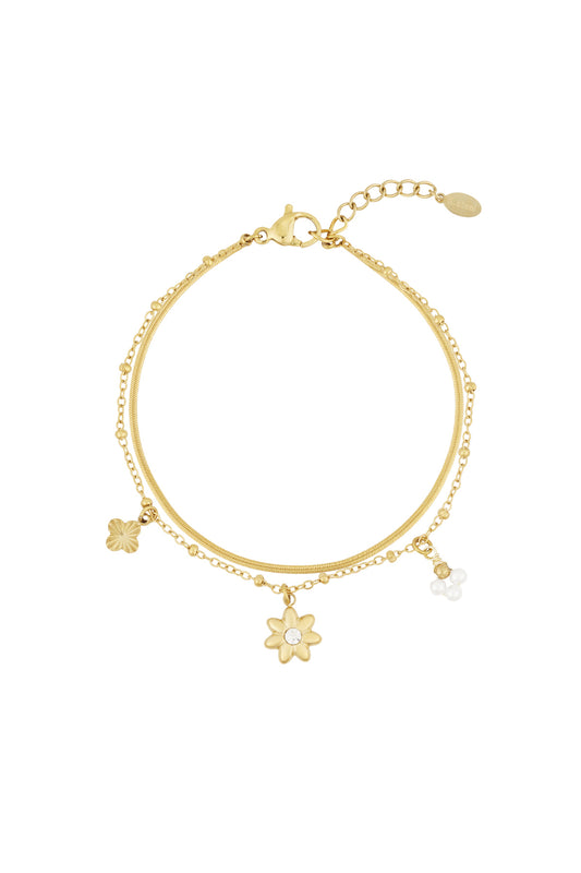 Gold plated layered charm bracelet with flower and pearl pendants isolated on white