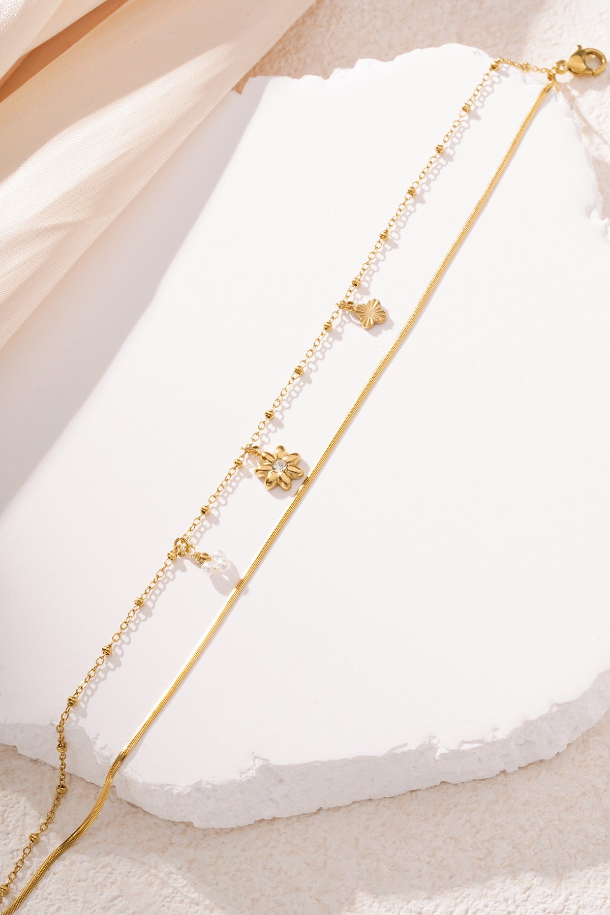 Gold floral charm bracelet with two chains layered on white textured surface