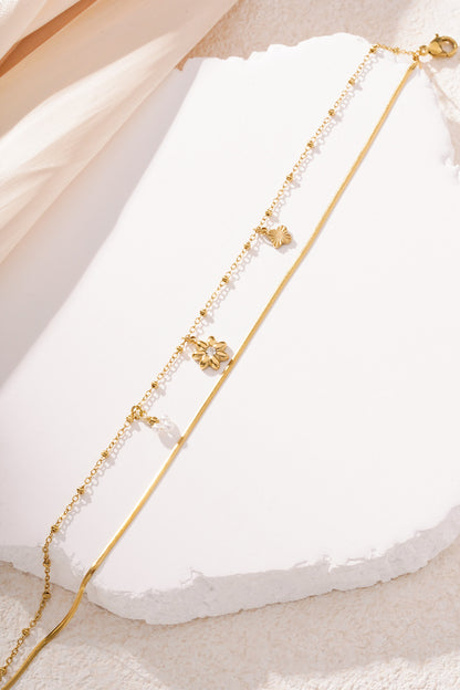 Gold floral charm bracelet with two chains layered on white textured surface