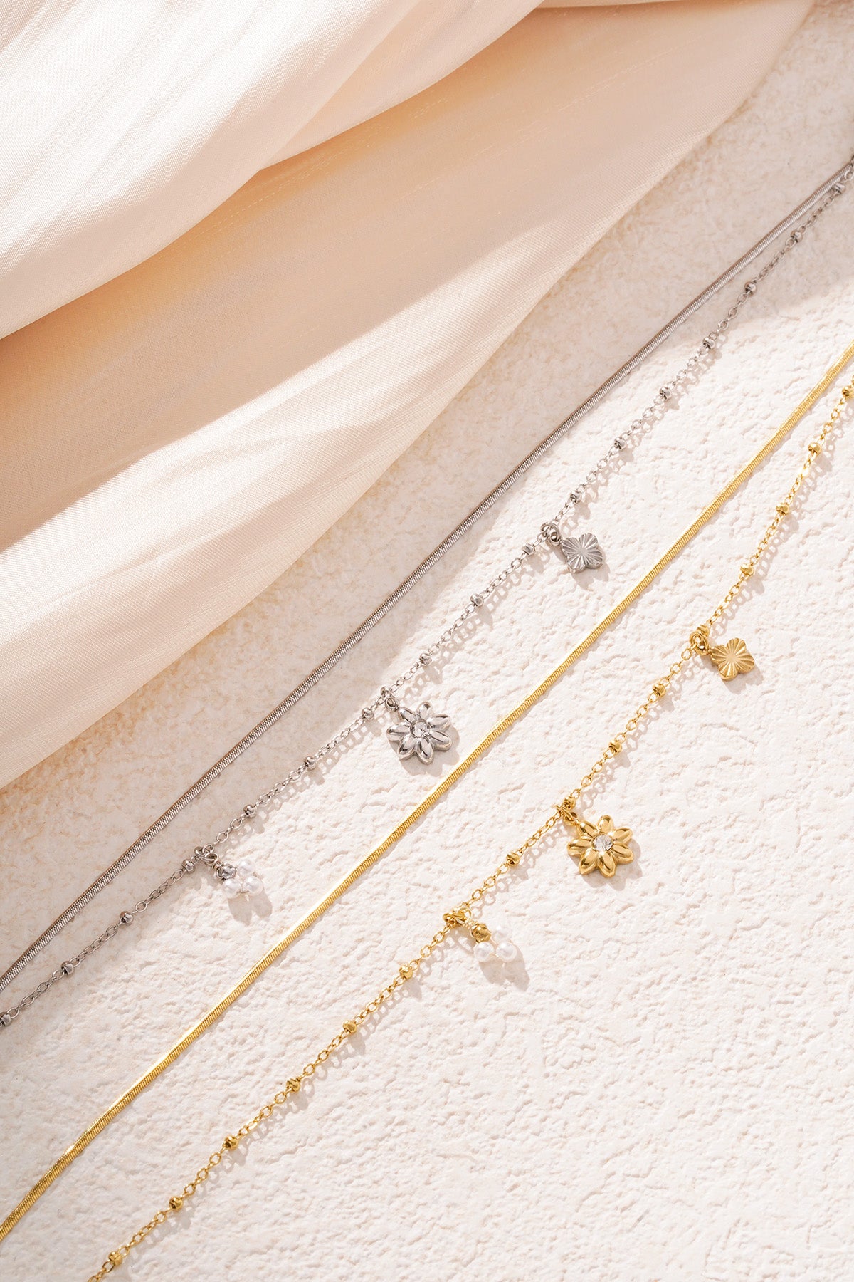 Close-up of gold and silver floral charm bracelets with pearl accents on white fabric and textured surface