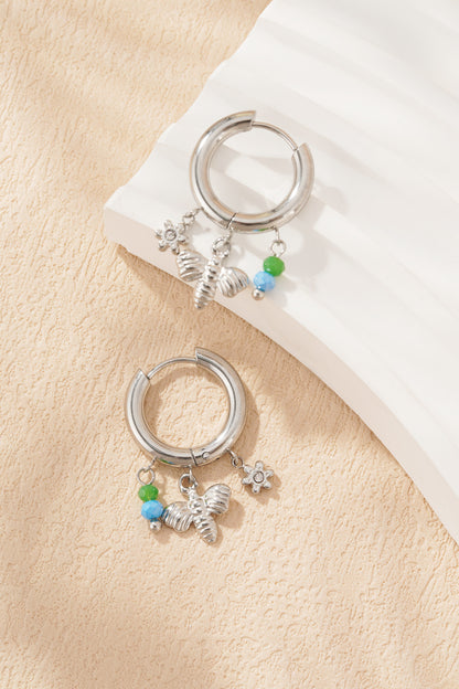 Silver charm hoop earrings with bee, flower charms and green-blue beads on white sculptured surface