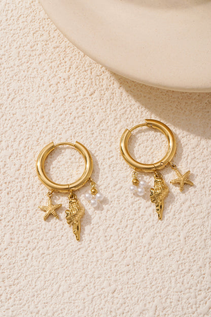 Gold charm hoop earrings placed on textured cream surface with soft lighting