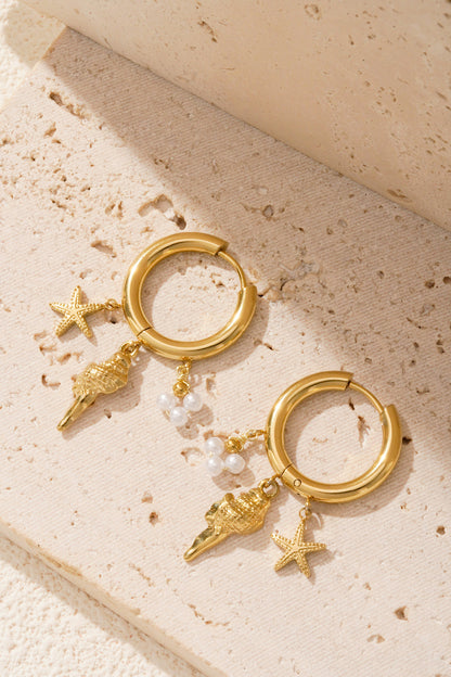 Close-up of gold charm hoop earrings with sea motifs on a minimal beige block background