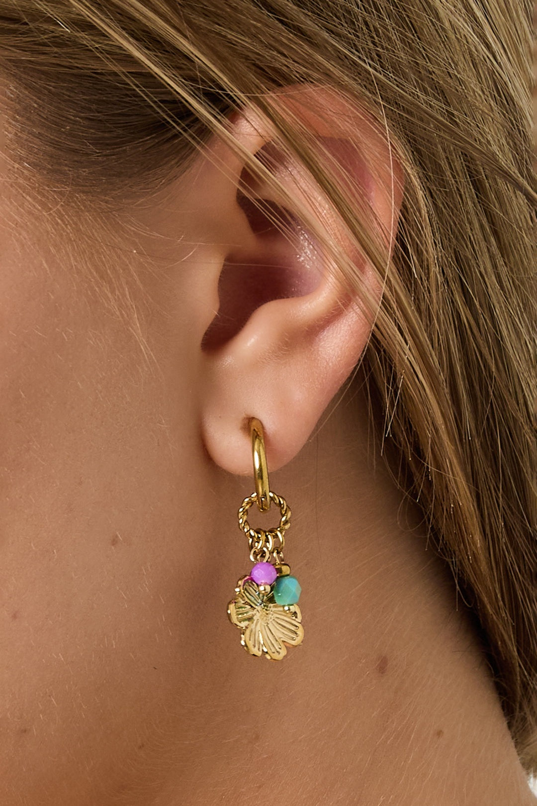 Close-up front view of woman wearing gold hoop earrings featuring flower charms and pink and turquoise beads