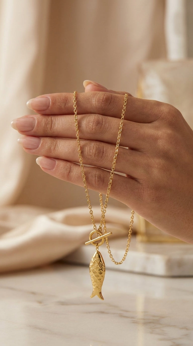 Gold Catching Vibes necklace featuring a fish charm pendant on a chain with a front toggle clasp.