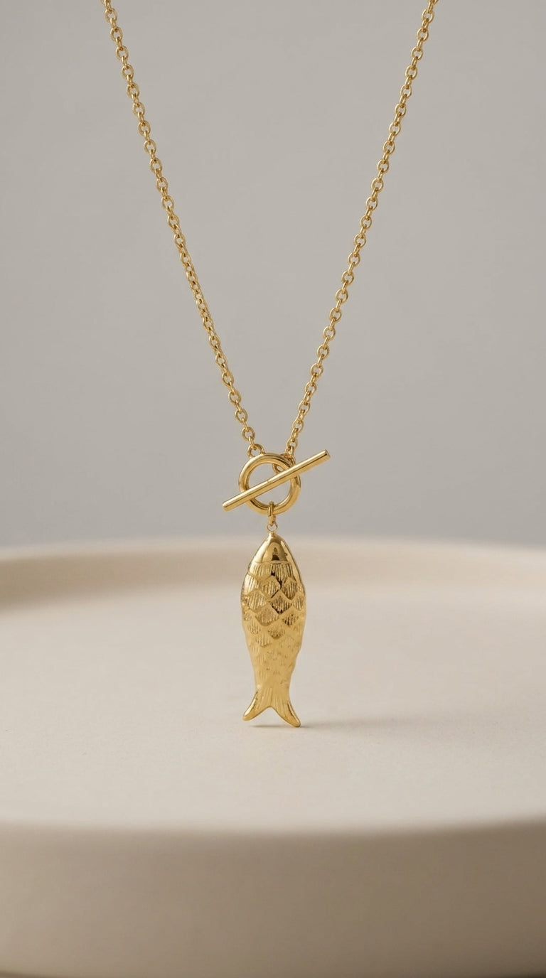 Gold Catching Vibes necklace featuring a detailed fish pendant hanging from a minimalist toggle clasp.