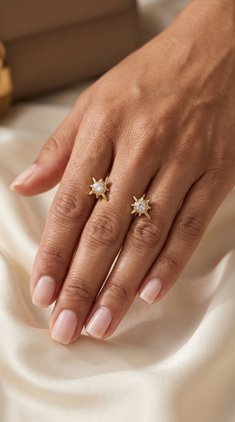Gold starburst rings with central clear crystals worn on two fingers against a cream satin background.