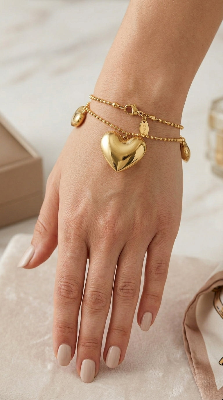 Gold double-strand beaded bracelet featuring a large, polished puffy heart charm and small heart accents.