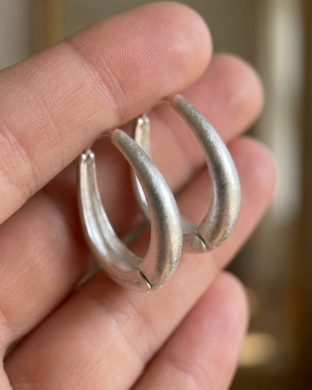 Chunky silver hoop earrings with a brushed texture held gently in an open hand.