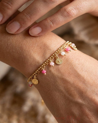 Two gold steel charm bracelets with pink beads and sunburst pendants worn on a wrist.