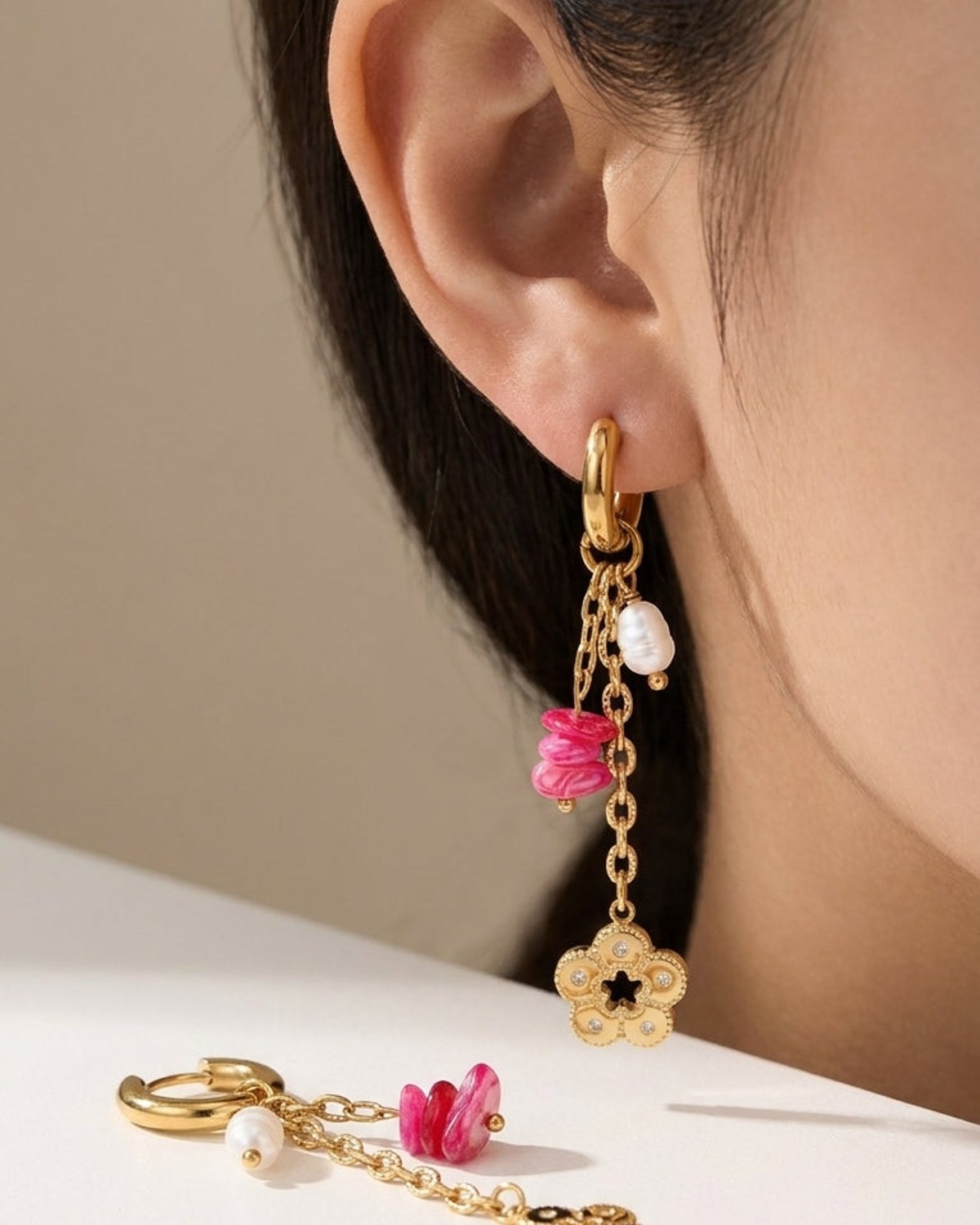 Chic gold drop earrings featuring dangling chains, white pearls, pink marbled beads, and a floral charm.