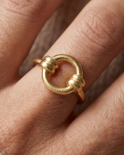 Matte gold ring featuring a central circle with dual-wrapped knot details on opposite sides.