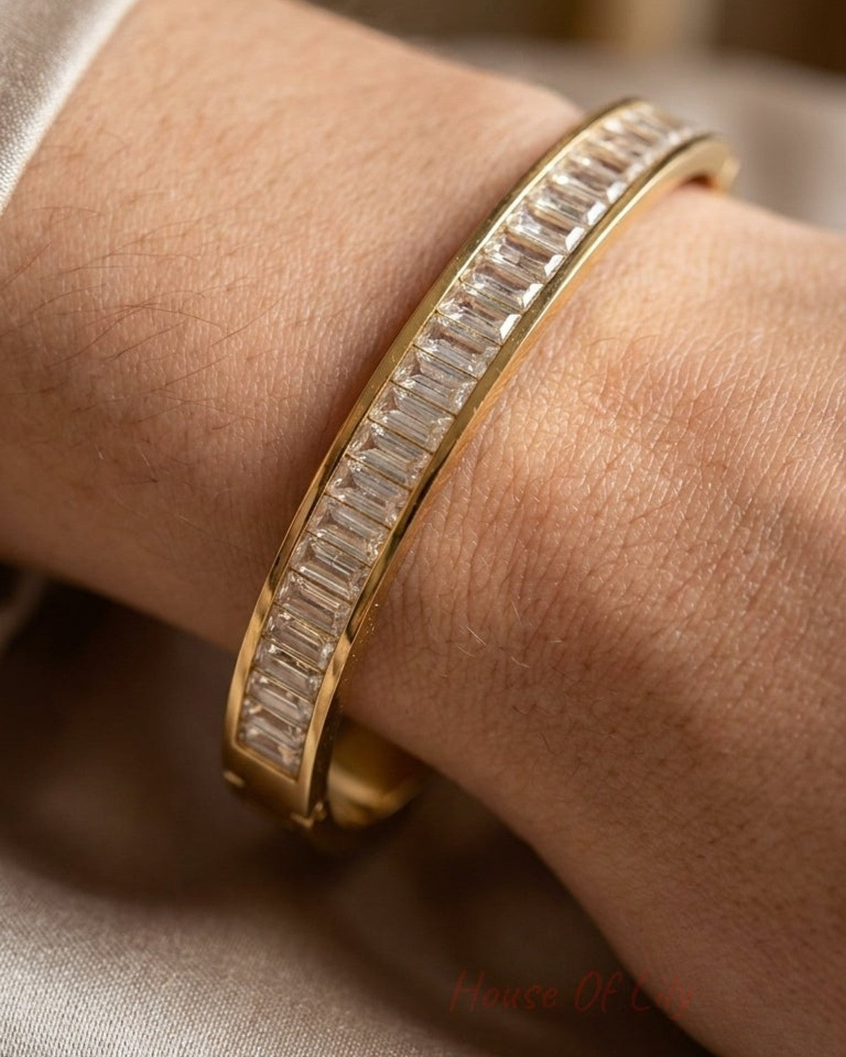 A gold bangle bracelet with a continuous line of baguette-cut diamonds on a wrist.