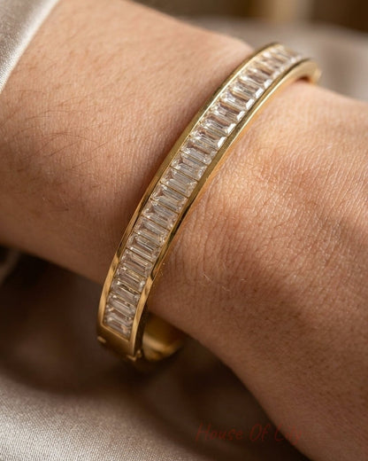 A gold bangle bracelet with a continuous line of baguette-cut diamonds on a wrist.