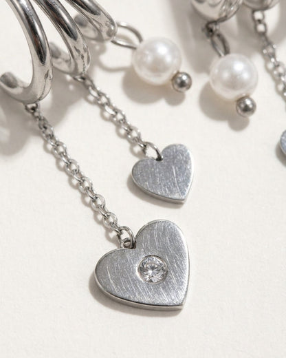Silver-tone earrings feature dangling heart charms with set zircon stones and pearls on chains.