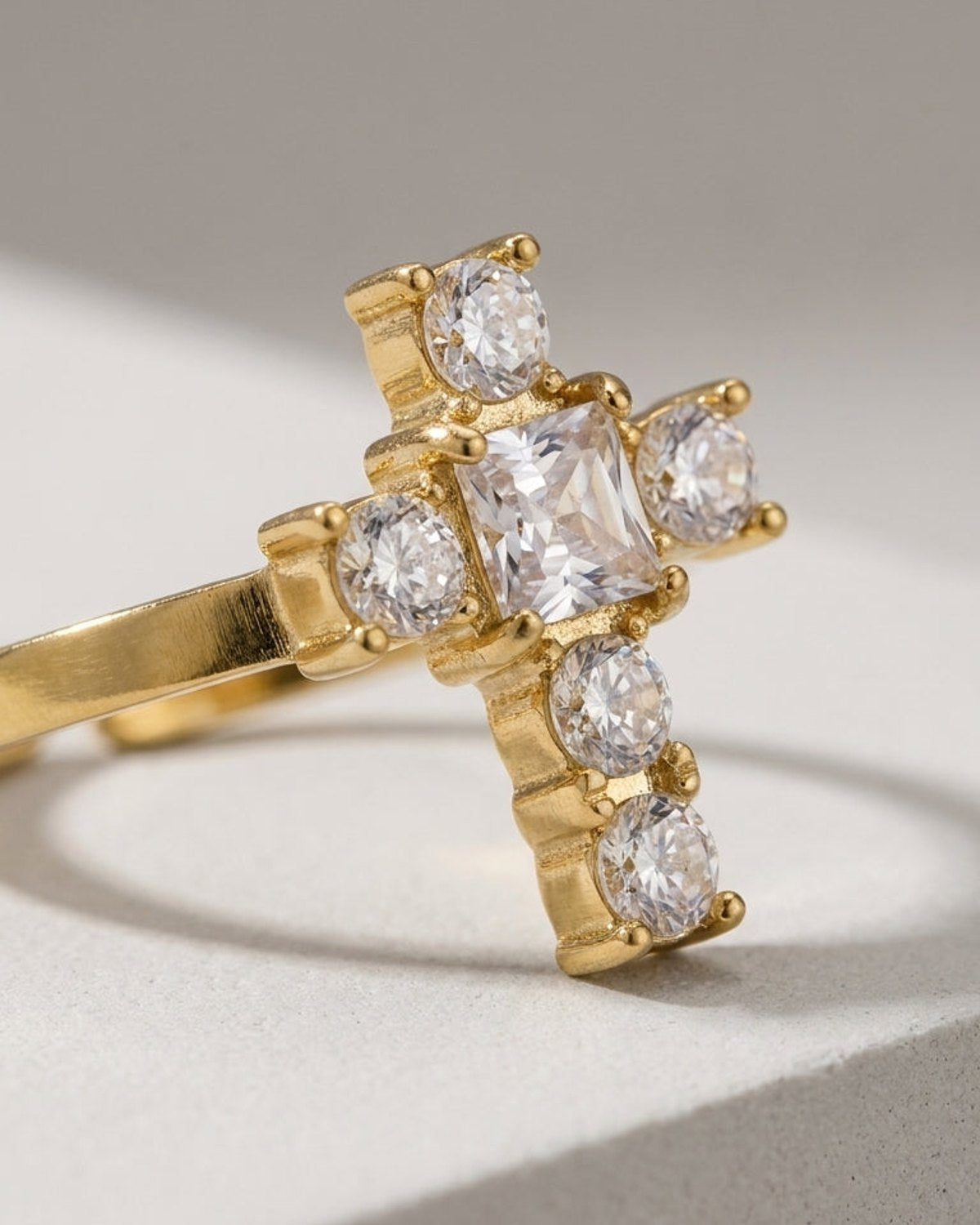 Gold ring featuring a cross-shaped centerpiece set with a central square stone and five round clear stones.