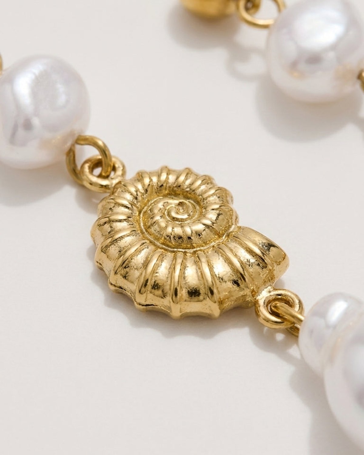 Gold nautilus shell charm dangling between white pearls on drop earrings.