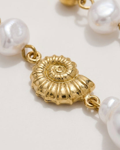 Gold nautilus shell charm dangling between white pearls on drop earrings.