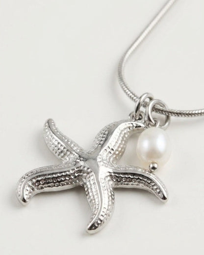 Silver-tone starfish pendant necklace with textured details and a hanging white pearl bead on a thin chain.