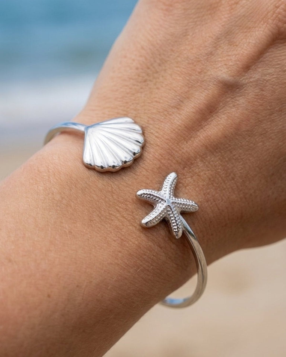 Silver open cuff bracelet on a wrist featuring a seashell on one end and a starfish on the other.