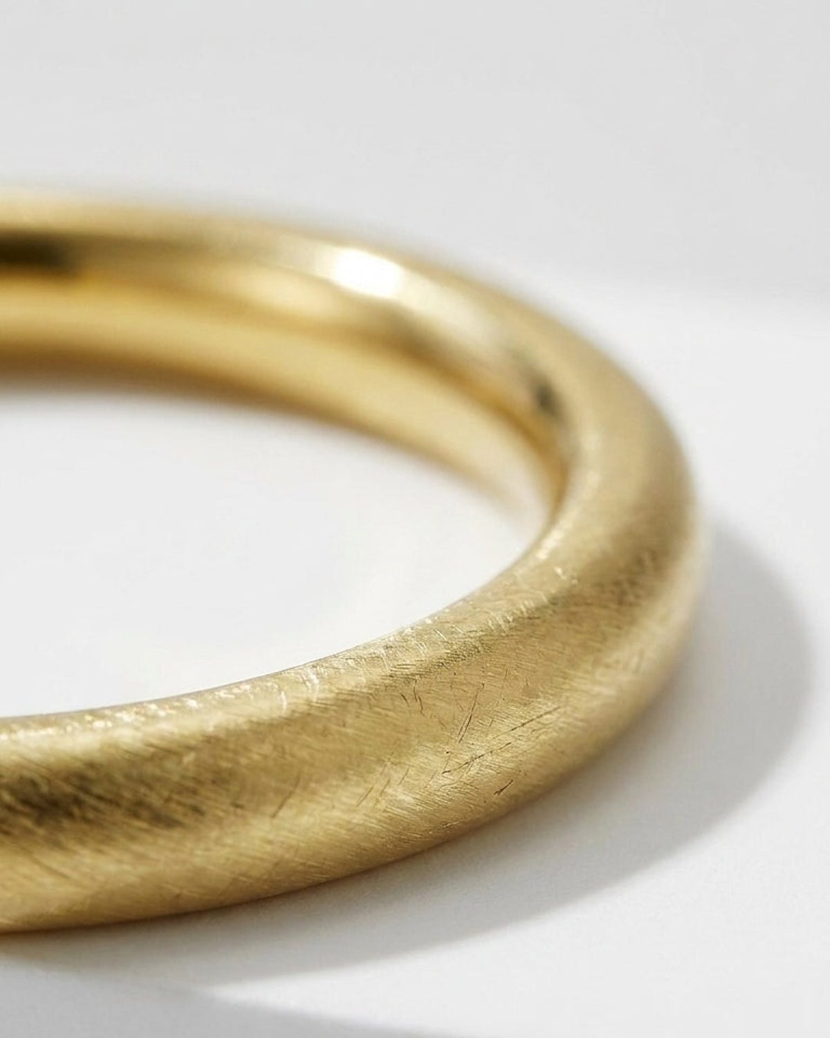 Thick gold bangle with a brushed, textured finish, shown close up on a light background.