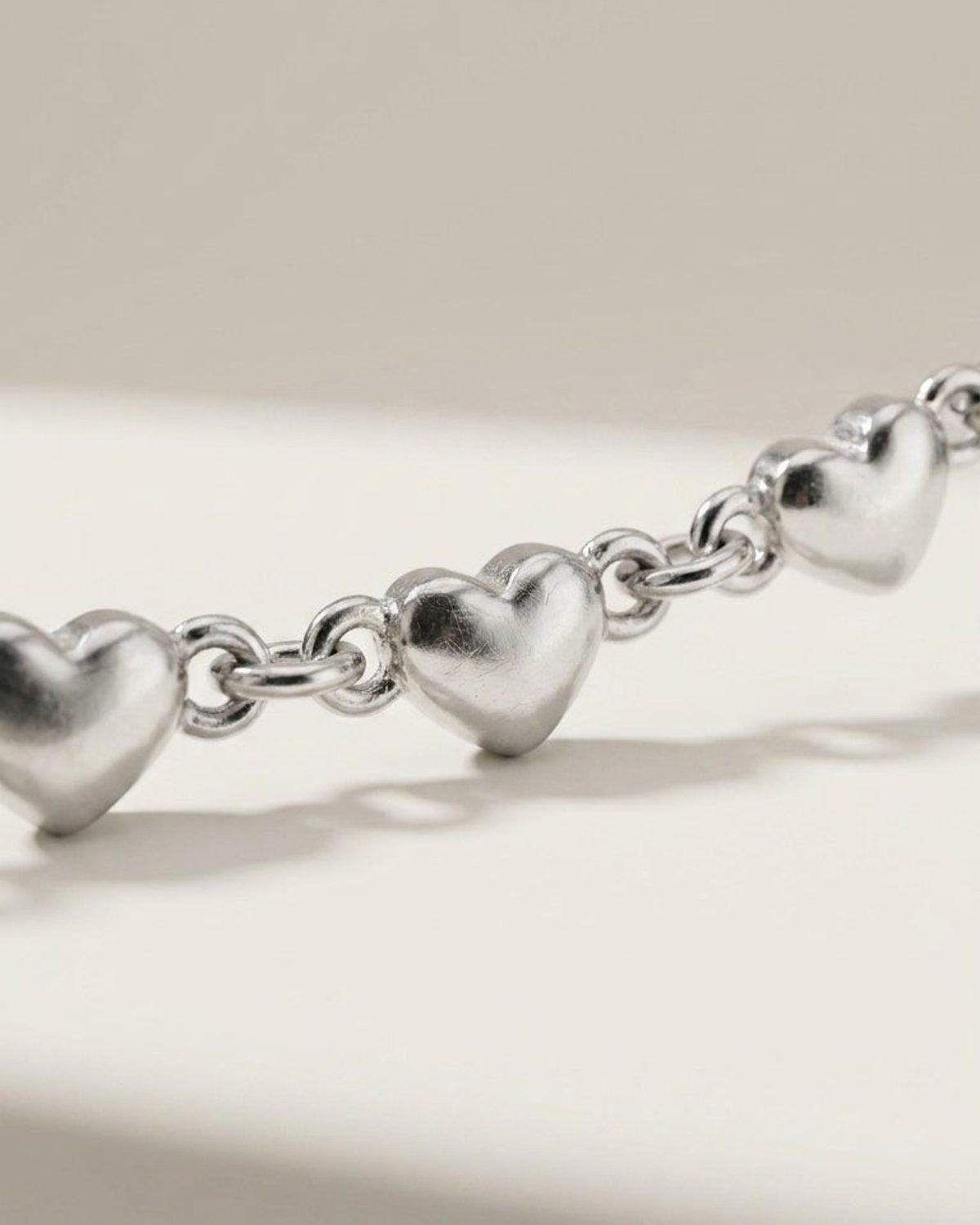 Delicate silver multi-heart chain bracelet with puffy heart charms linked by metal rings.