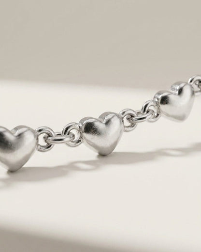 Delicate silver multi-heart chain bracelet with puffy heart charms linked by metal rings.