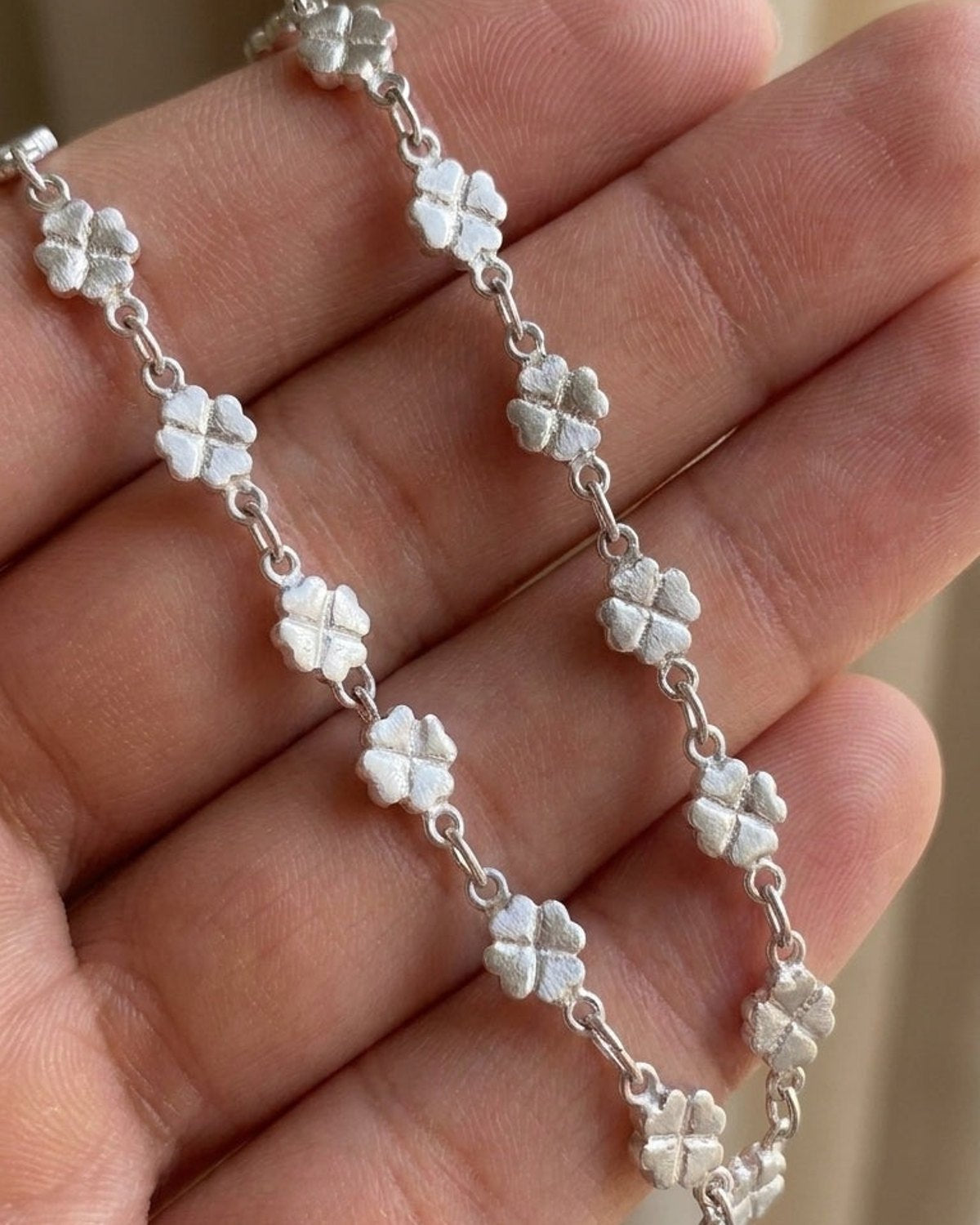 A dainty silver lucky clover chain bracelet with textured matte four-leaf clovers linked together.