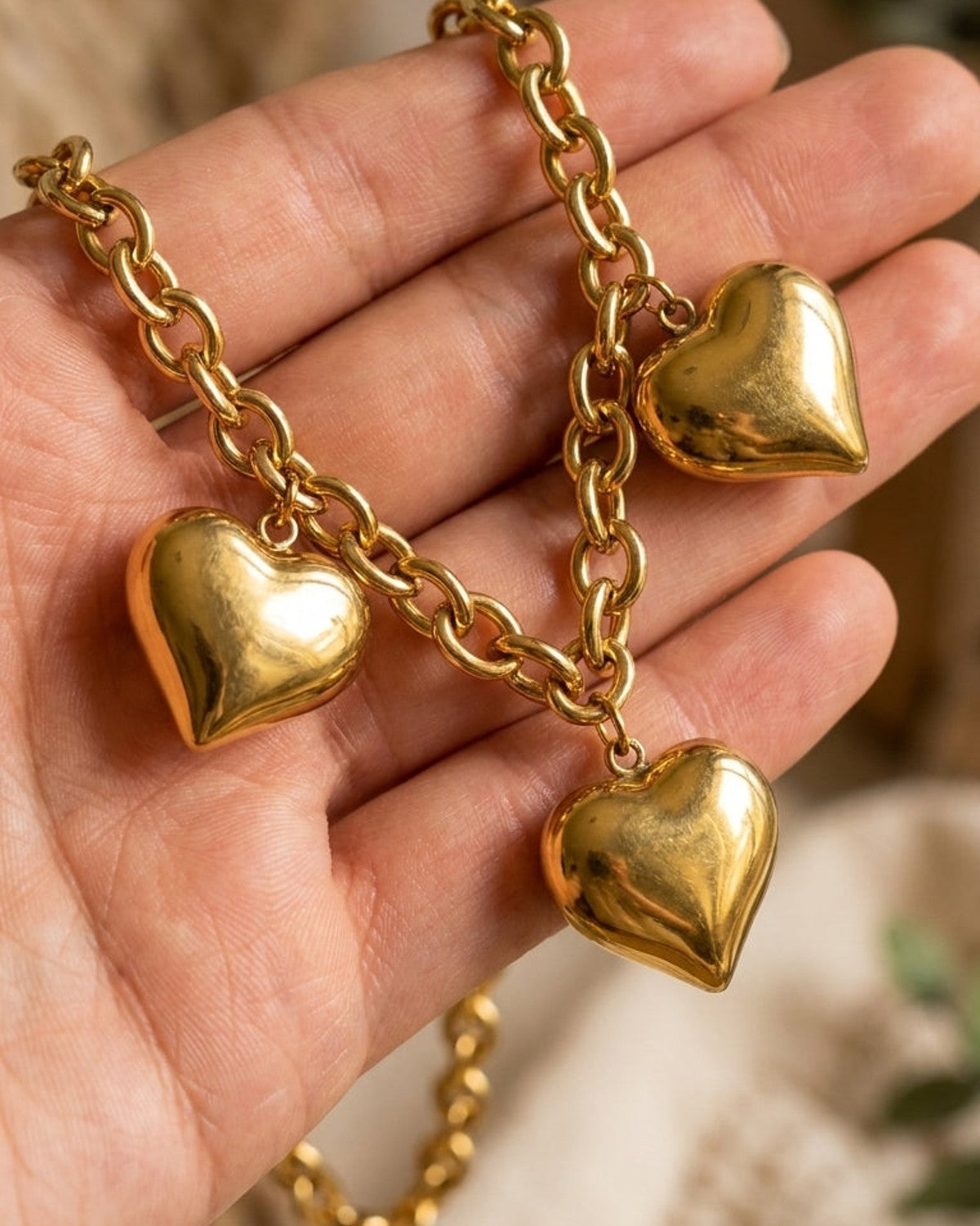 Gold heart pendant necklace on a thick link chain, held in a person's open hand.