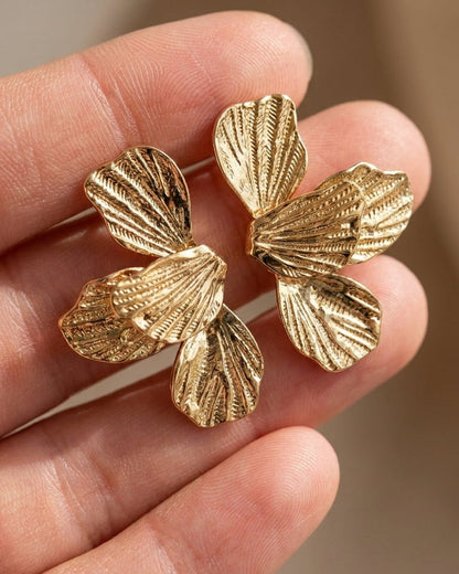 Textured gold Flower Drop Earrings shaped like blooming flowers with detailed, layered petal designs held in a hand.