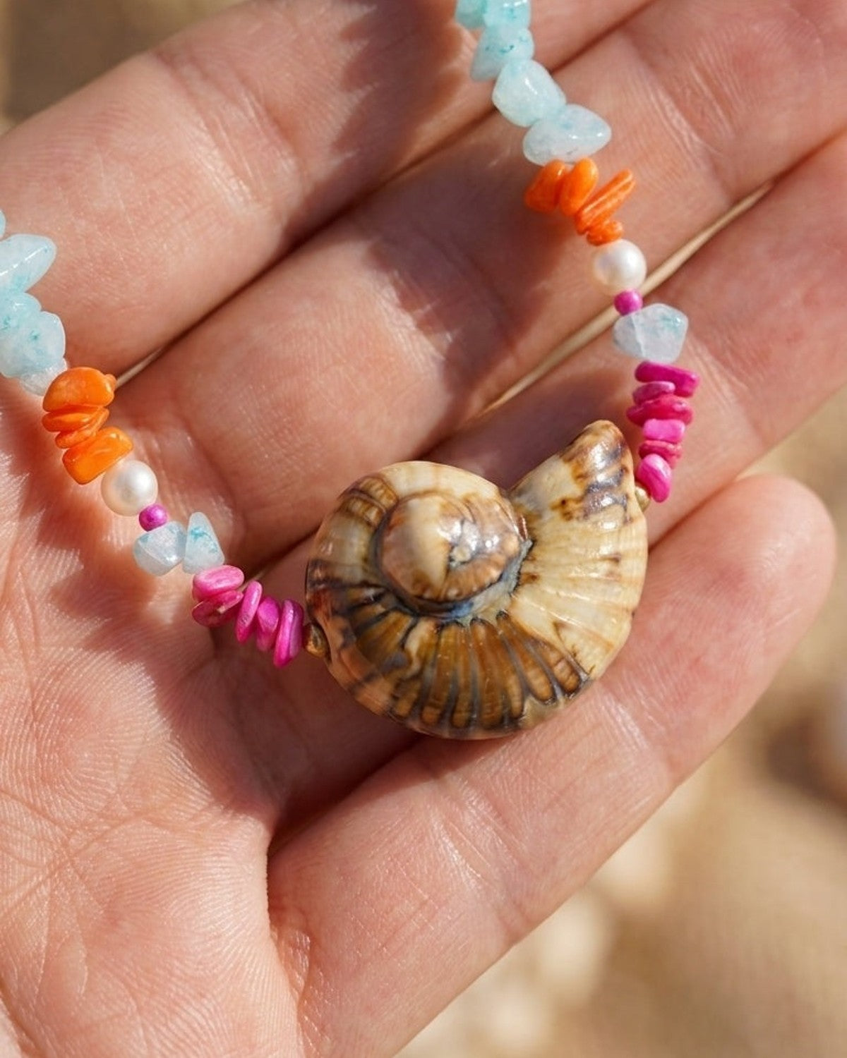 House Of Lily beaded necklace featuring a central brown shell and colorful chipped stones resting in a hand.