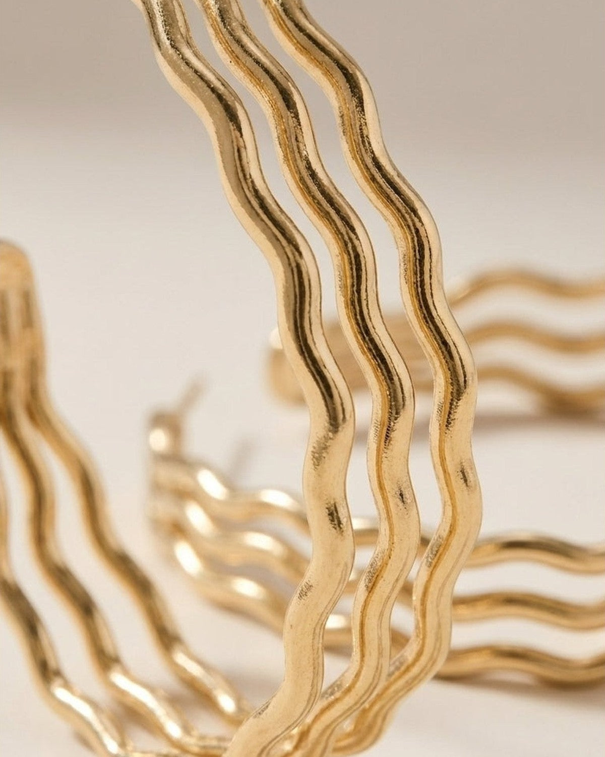 Close-up of gold-toned triple-layered wavy hoop earrings against a neutral background.