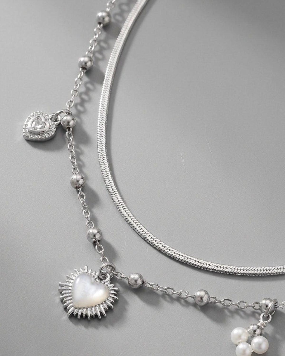 Silver double-strand coquette necklace with a mother-of-pearl heart charm, rhinestones, and pearl accents.