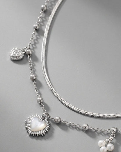 Silver double-strand coquette necklace with a mother-of-pearl heart charm, rhinestones, and pearl accents.