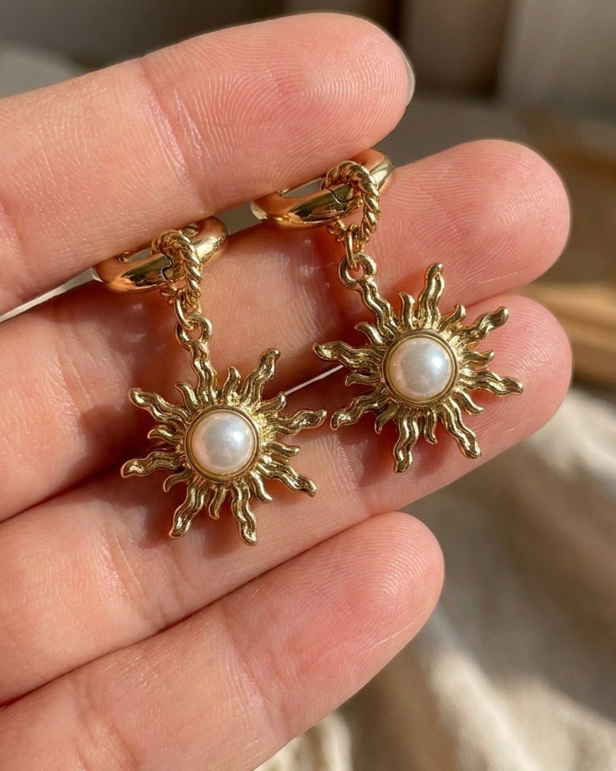Sunlit Loop gold hoop earrings with textured sunburst charms centered with white pearls held in fingers.